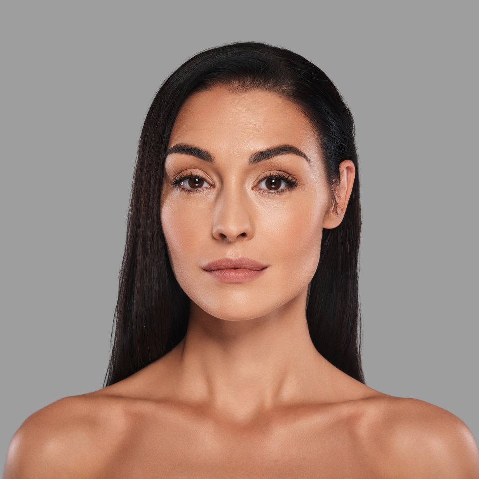 Glowing with natural beauty. Attractive young woman looking at camera and smiling while standing against grey background