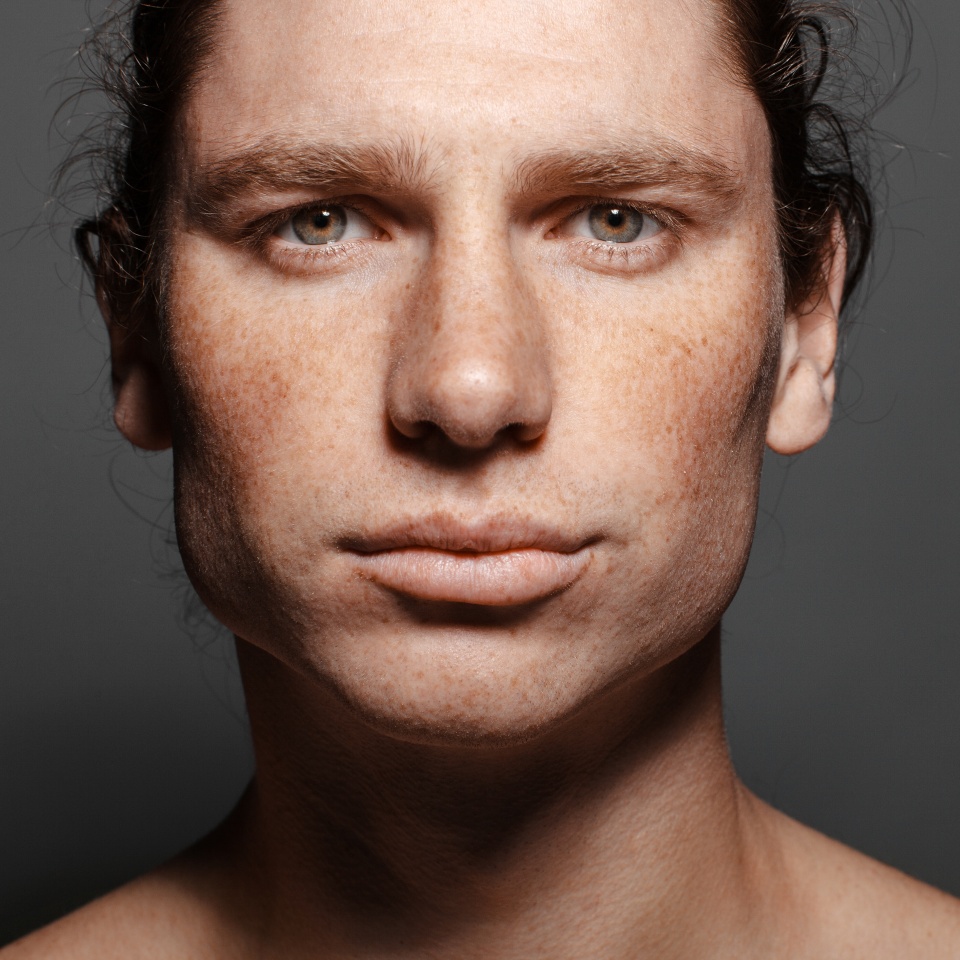 Portrait of a handsome long-haired man with drawn hair and freckles. Dark gray background