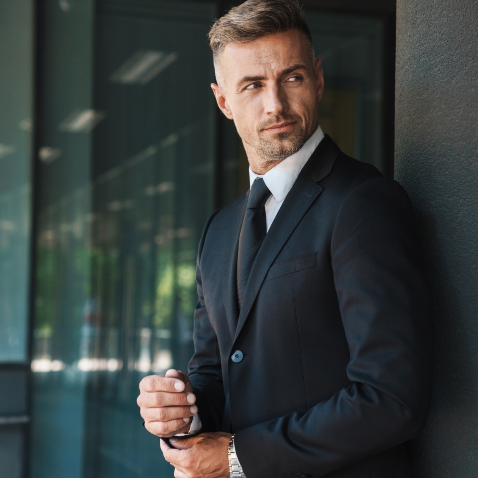 Photo of a serious mature handsome grey-haired business man outdoors at the street near business center.