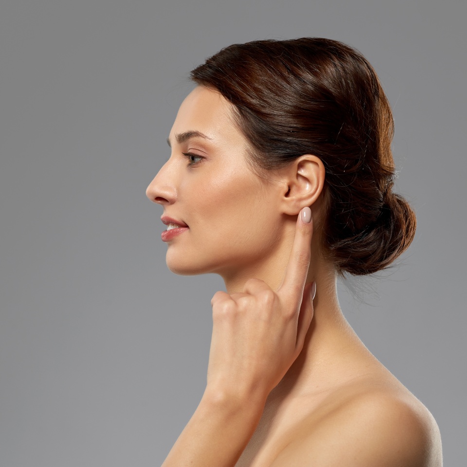 hearing, people and beauty concept - beautiful young woman pointing finger to her ear over grey background