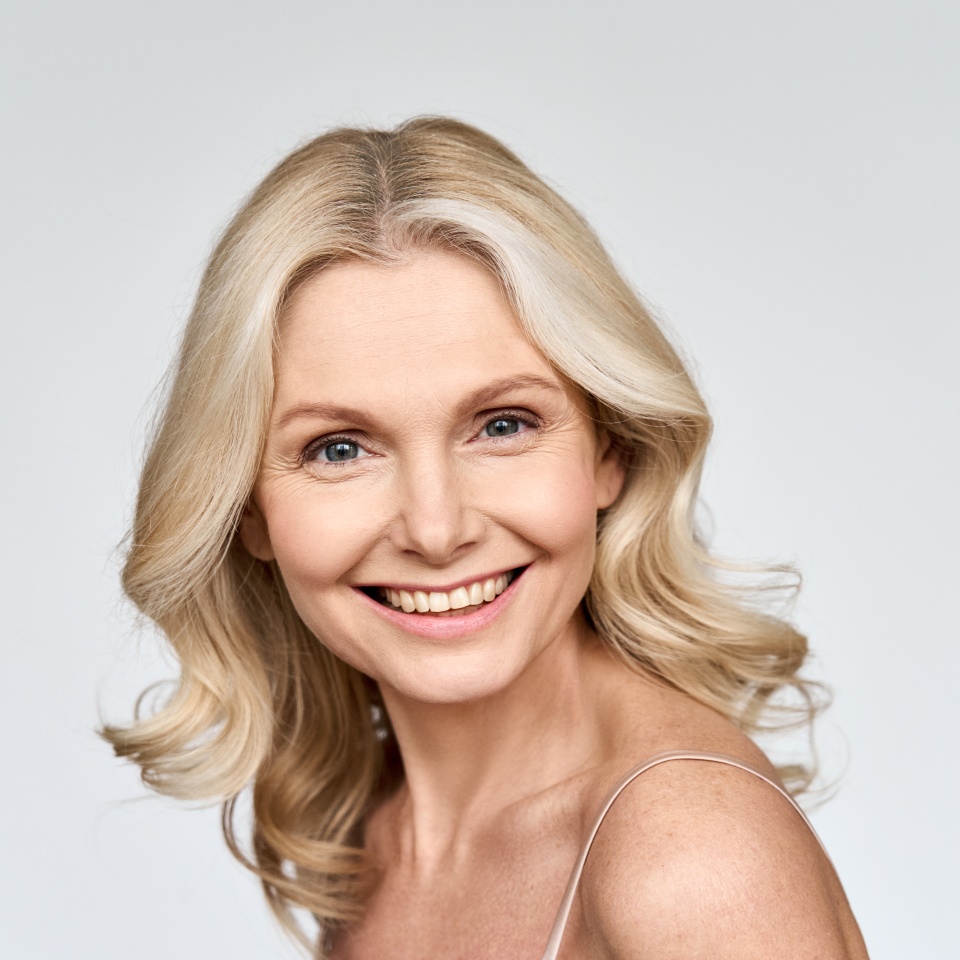 Gorgeous happy smiling middle 50s age woman looking at camera portrait isolated on white background. Face tighten rejuvenating skin care products advertising concept.