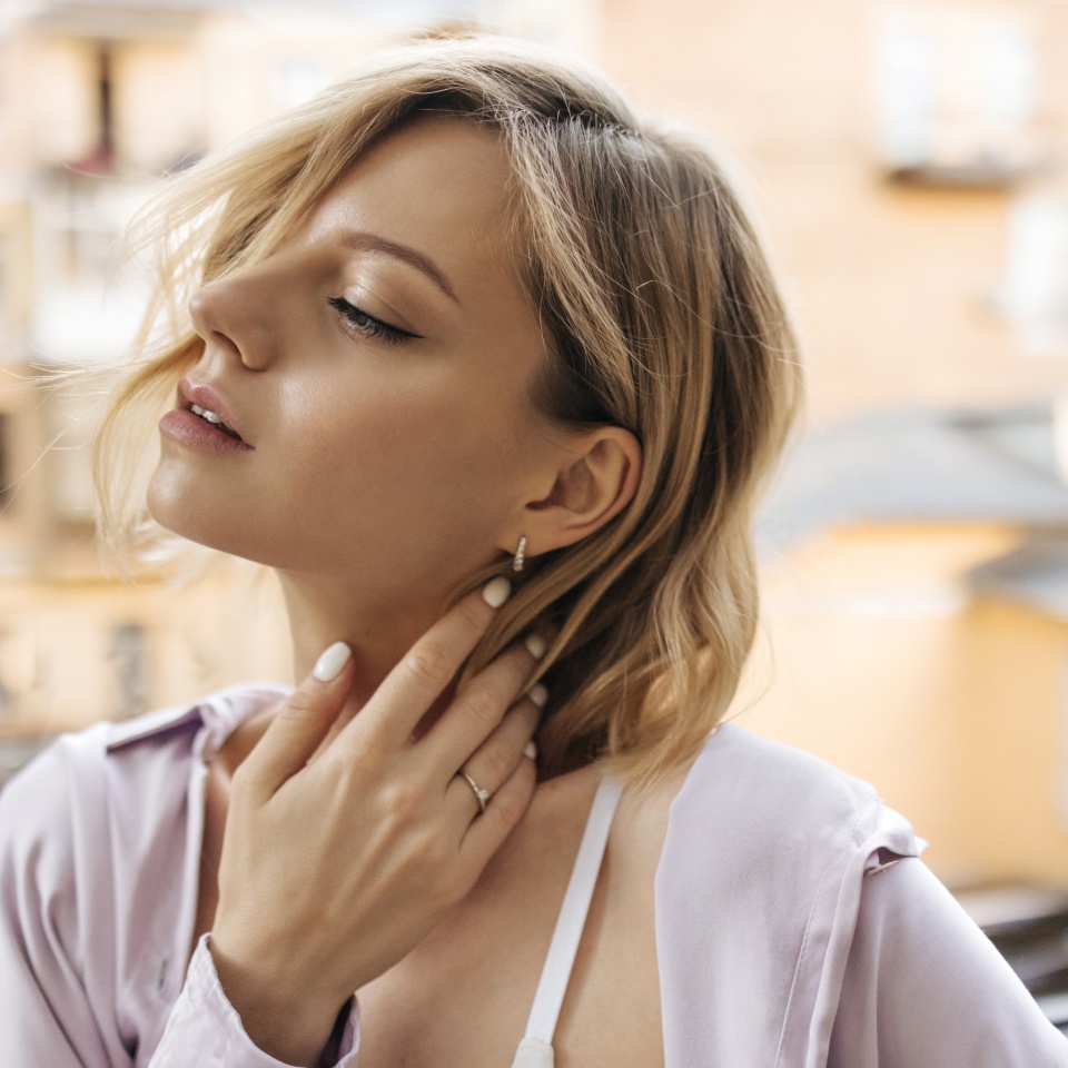 In profile close-up gentle image of young caucasian woman with languid look outdoors. Short-haired blonde tucked her hair behind ear, dressed in casual light clothes.