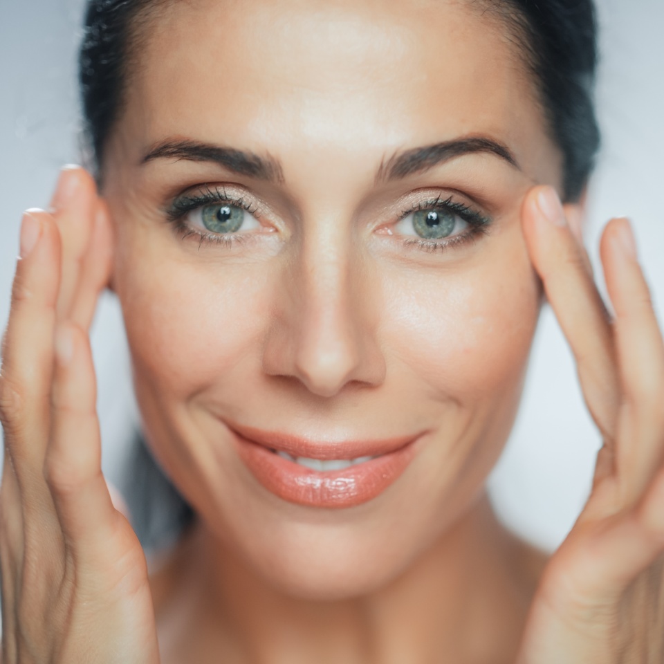 Beautiful Caucasian Woman Touches Her Perfect Face with Soft Skin, Smiling. Female Enjoying Her Beauty, High Self Esteem, Wellness. Natural Cosmetic Skincare Products. Portrait on Isolated Background