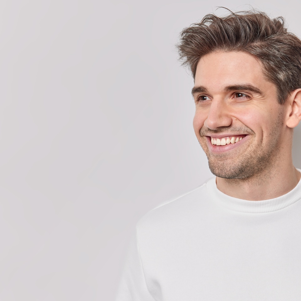 Horizontal shot of handsome pleased European man looks away with happy smile on face dressed casually feels satisfied notices something into distance isolated over white bacground blank copy space