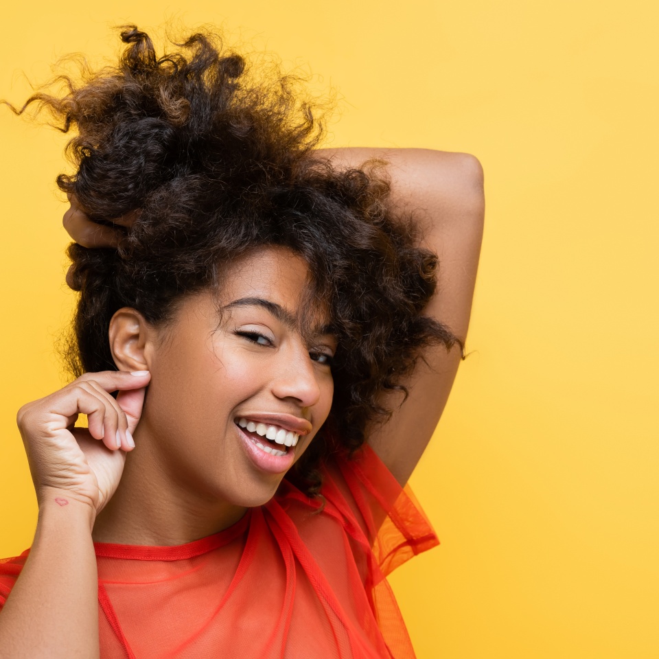 smiling african american woman showing listening gesture while touching earlobe isolated on yellow