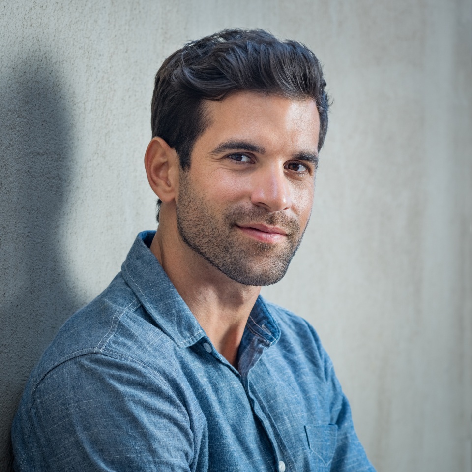 Handsome young man posing on grey background. Portrait of satisfied businessman against grey wall. Close up face of fashionable latin man on grey background.