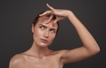 Close up portrait of displeased lady with naked shoulders checking the existence of frown lines. Isolated on gray background