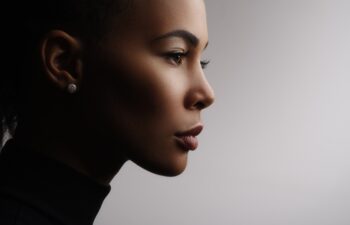Closeup fashionable portrait of a metis young woman with perfect smooth glowing skin, full lips, collected hair and long neck. Studio photo of an african american female model face, profile