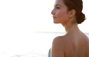 Close up side portrait of a young woman contemplating the scene, standing on a beach and enjoying the blue sea and sky at sunset during a summer vacation.