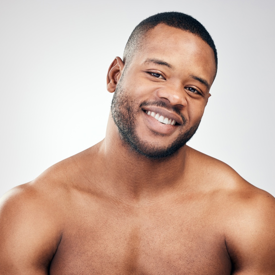 Studio, portrait and skincare of black man for wellness, healthy skin and pamper with cosmetics. Male model, smile and natural glow for beauty, treatment results and confidence by white background