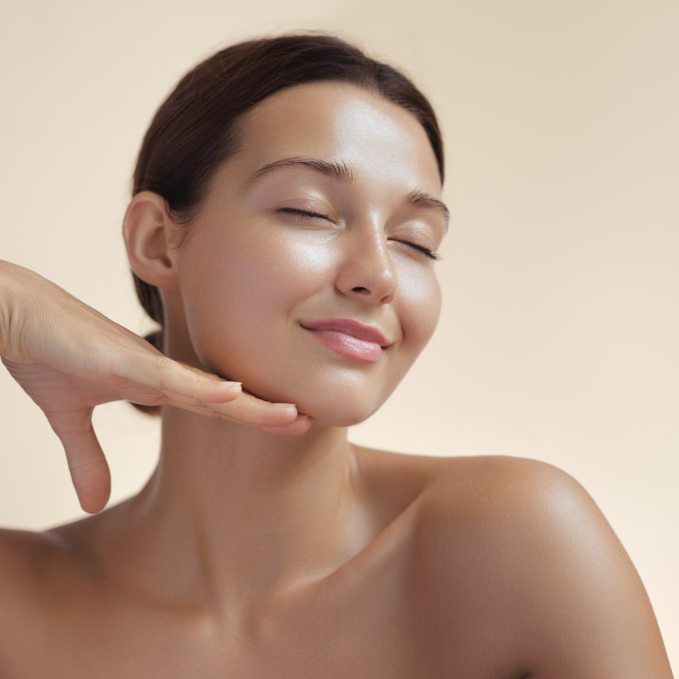 High-quality photo of skincare and cosmetics concept with copy space for text. Natural beauty woman woman with radiant, glowing skin closes her eyes and gently touches her face with her hand, creating