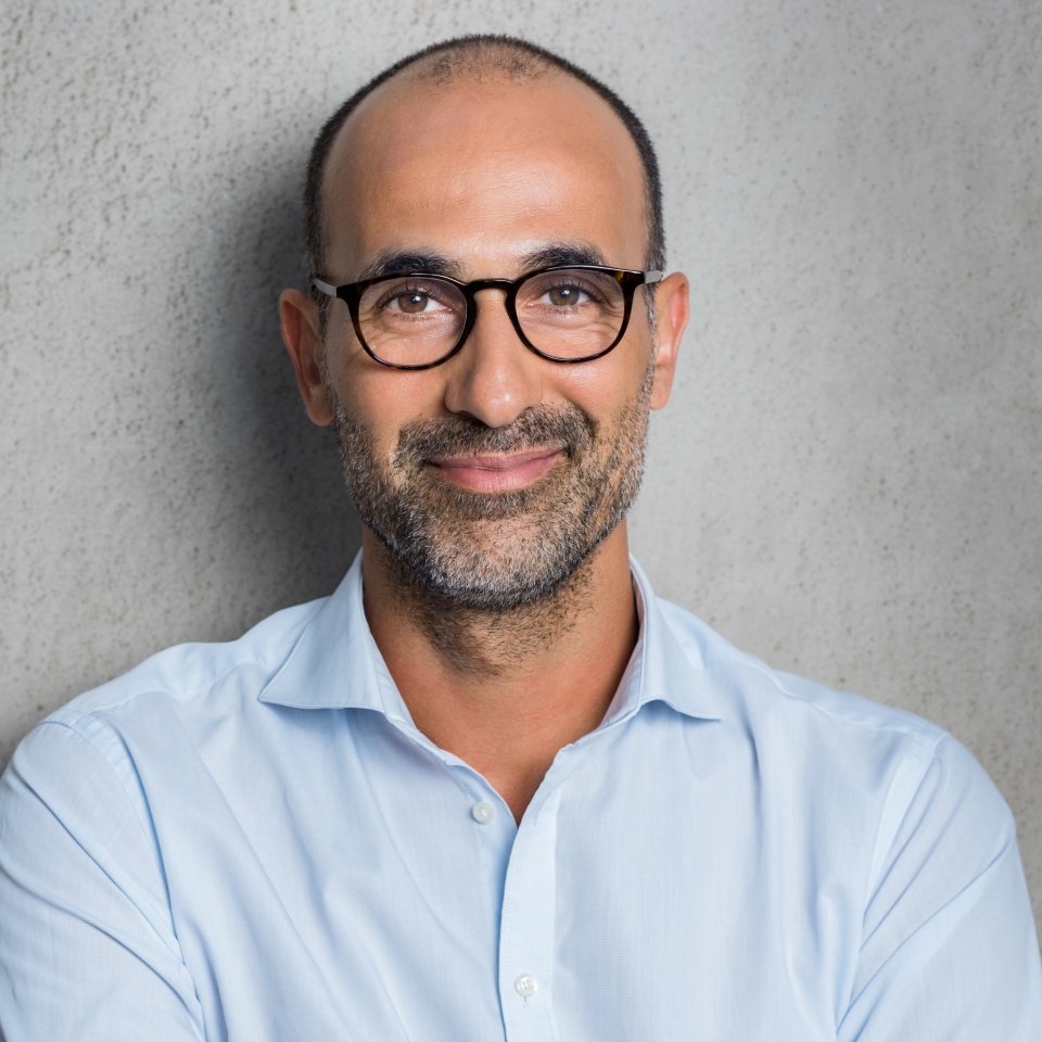 Portrait of a mature businessman wearing glasses on grey background. Happy senior latin man looking at camera isolated over grey wall with copy space. Close up face of happy successful business man.
